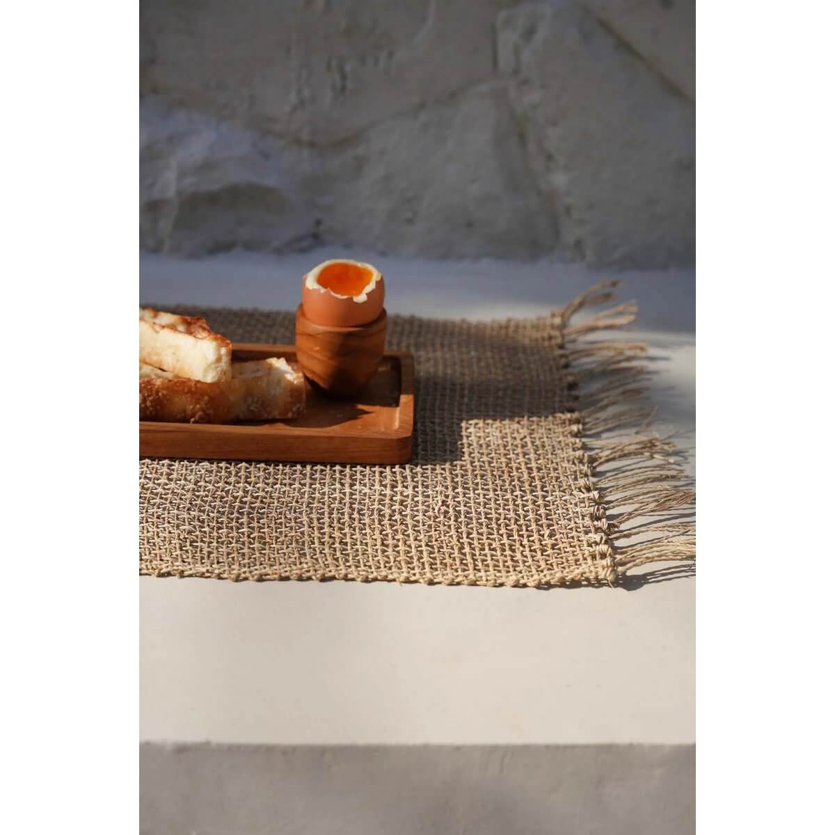 Bohemian teak root egg cup holding soft-boiled egg, on a rustic woven placemat.