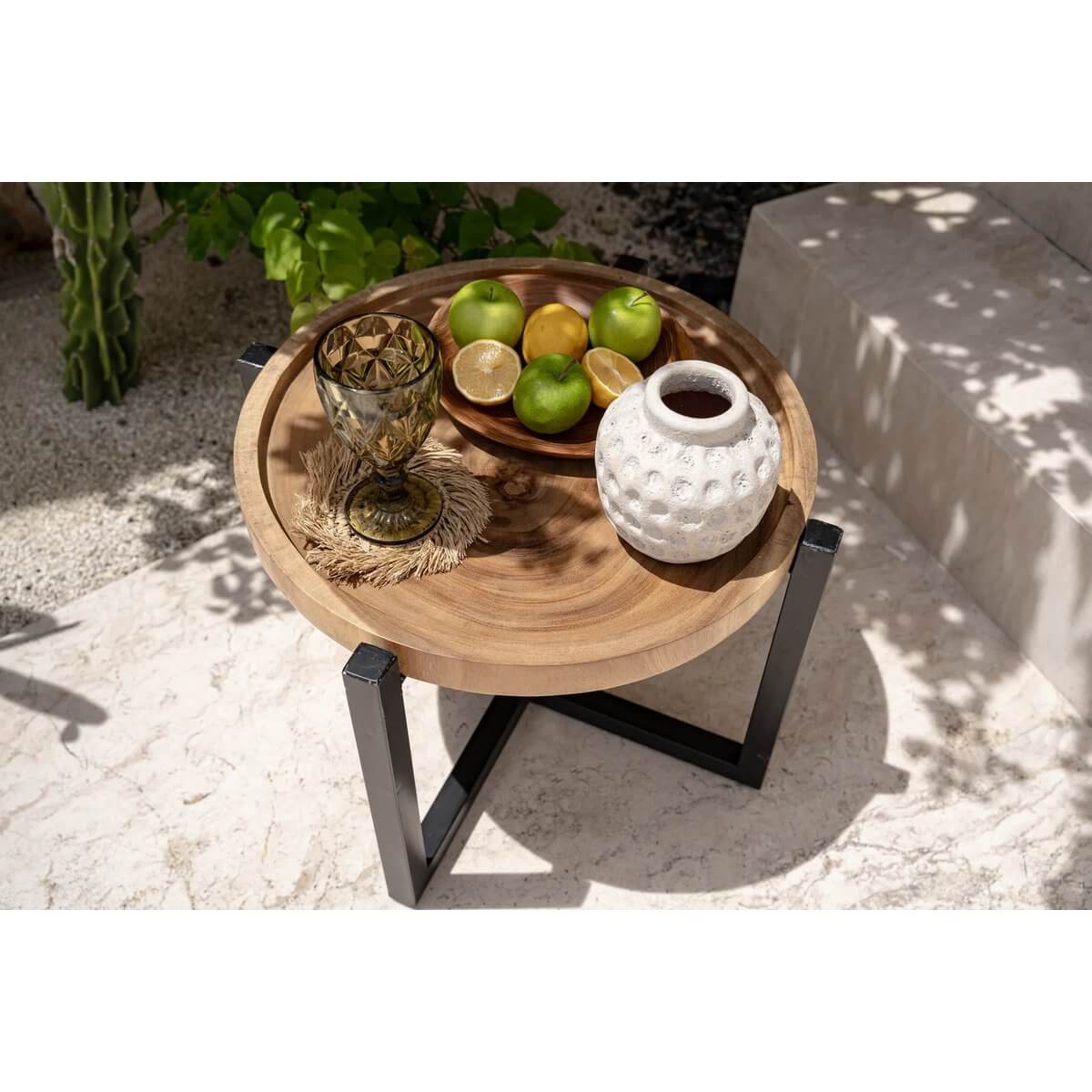 Round teak wood table with decorative white vase, glass, and fruit, perfect for Bohemian outdoor settings by Bazar Bizar Living.