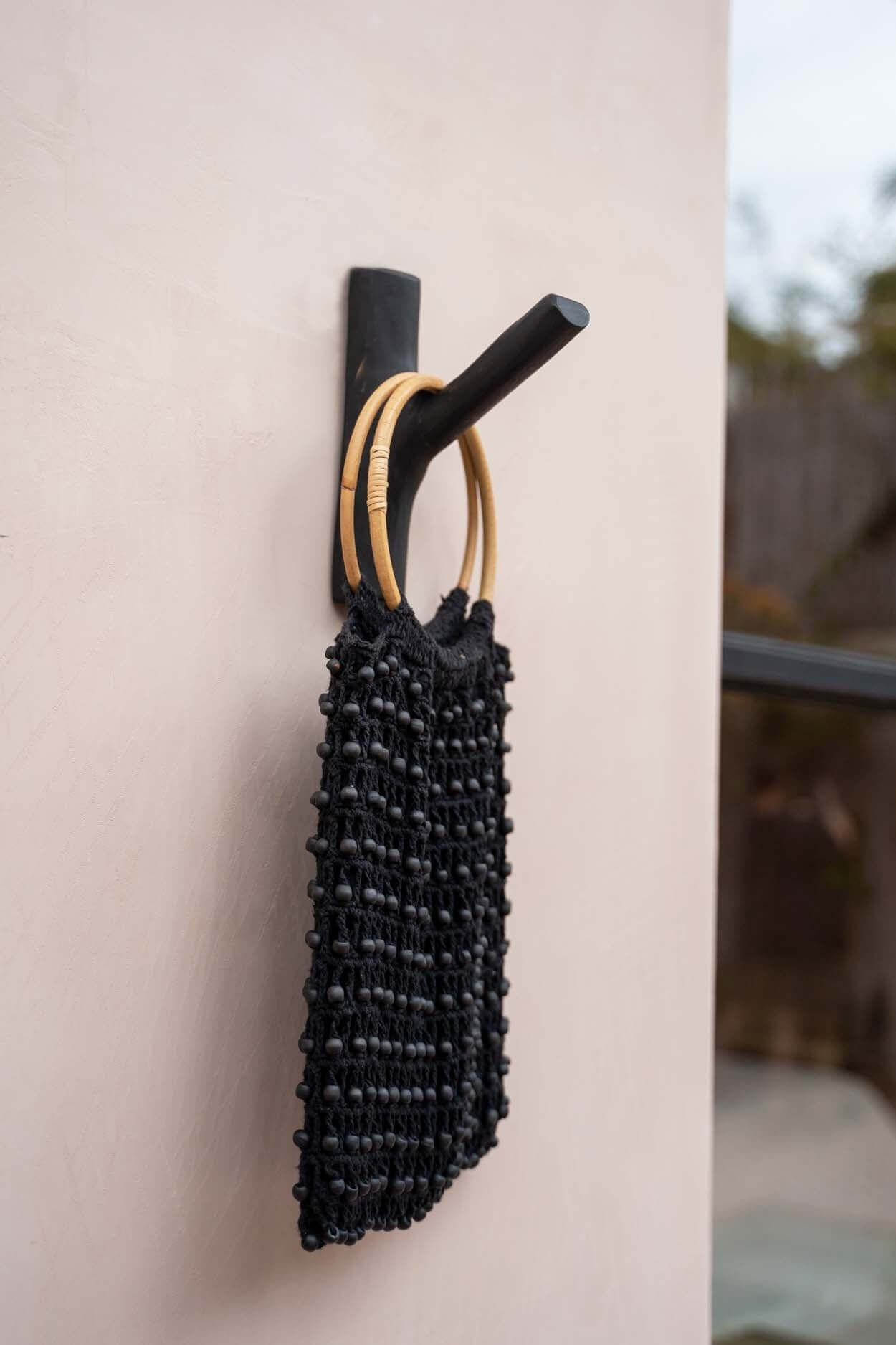 Zwarte teak houten haak "Kapstok The Hook" met decoratieve tas, perfect voor een kust-sfeer in elke kamer.