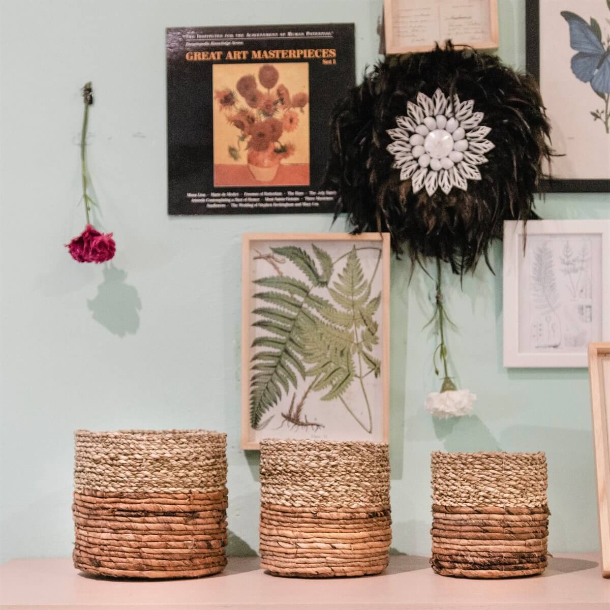 Drie handgemaakte zeegrasmanden BHINNEKA in verschillende maten voor decoratie en opslag, tegen een groene wand met kunst en bloemen.