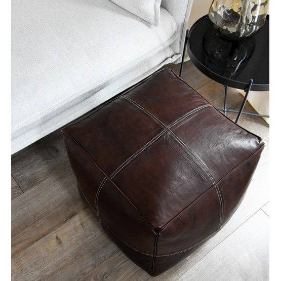 Bruine leren poef, modern vierkant design, geplaatst naast een bank in een woonkamer met houten vloer.