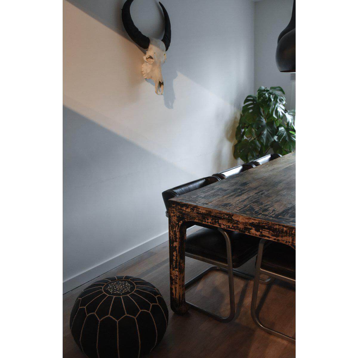Marokkaanse handgemaakte leren poef in donkerbruin in een boho-stijl interieur met vintage tafel en groen blad. Perfect voor woonkamer.