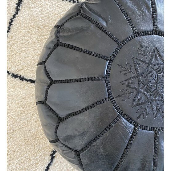 Zwarte Marokkaanse leren poef op beige tapijt, perfect voor decoratie, voetenbank of kinderzitplek. Handgemaakt met boho-stijl flair.