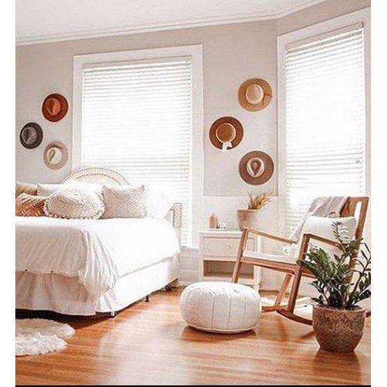 Knusse slaapkamer met witte leren poef, houten schommelstoel en hoedenmuur voor een boho sfeer.