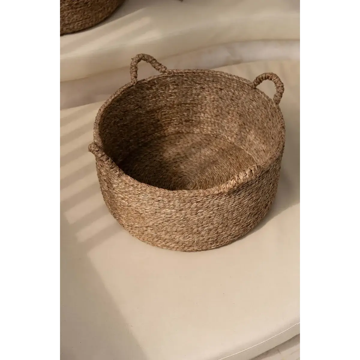 Eco-friendly woven seagrass basket with four handles, perfect for storing laundry, towels, or toys in boho chic interiors.
