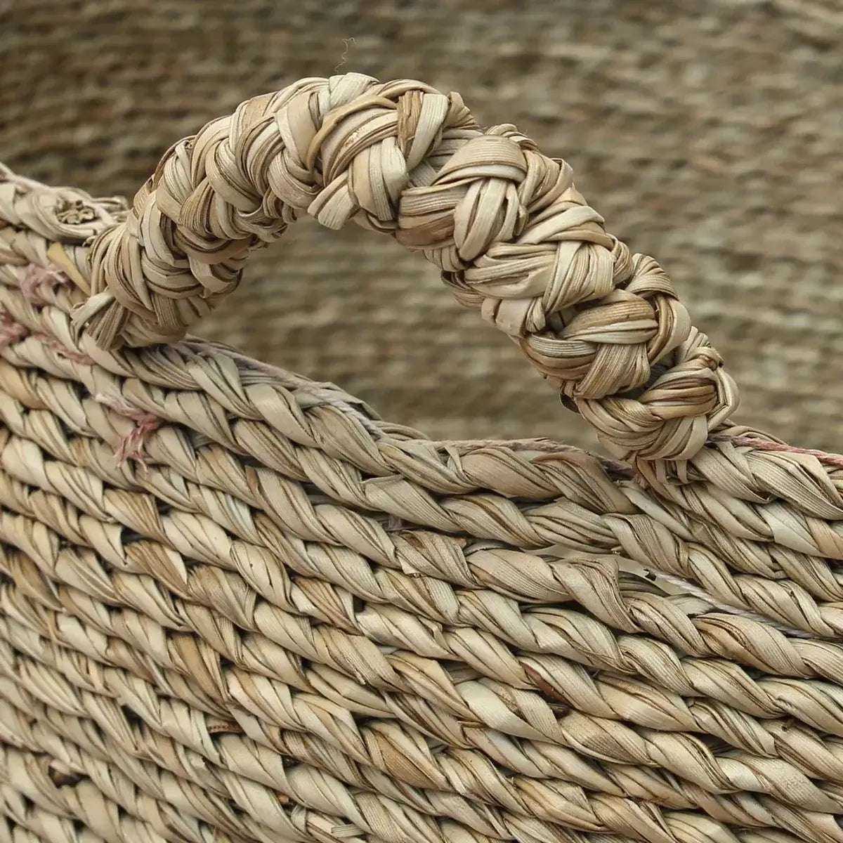 Close-up of woven sea grass basket handle on Les Quatre Mains Baskets, perfect for laundry, towels, or toys. Boho chic style.