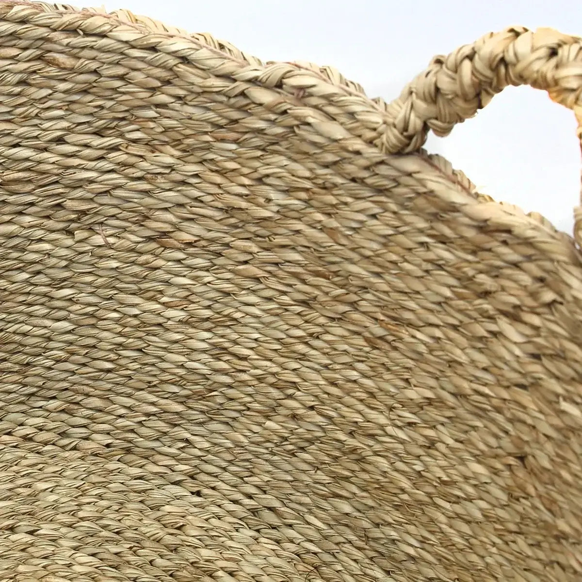 Close-up of woven seagrass basket texture with handle, ideal for laundry or storage in boho chic interiors.
