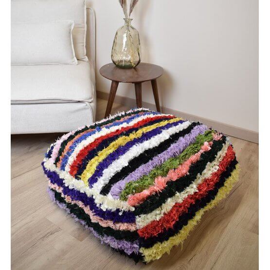 Kleurrijk Marokkaans Boucharouite-vloerkussen handgemaakt van gerecycled textiel, naast een moderne fauteuil.