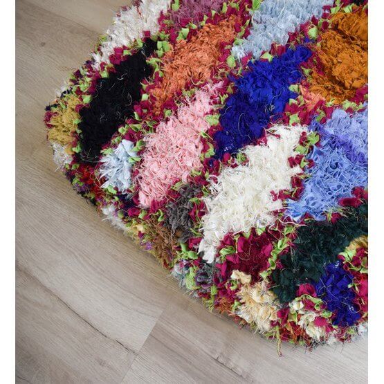 Vibrant Marokkaans Boucharouite-vloerkussen op houten vloer, kleurrijk en handgemaakt uit gerecycled textiel.