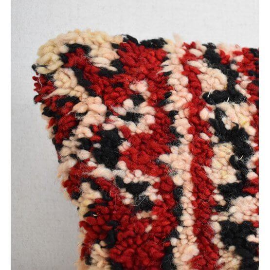 Close-up van een uniek handgemaakt Marokkaans kussen gemaakt van vintage Berberkleed in rood, zwart en crème tinten.