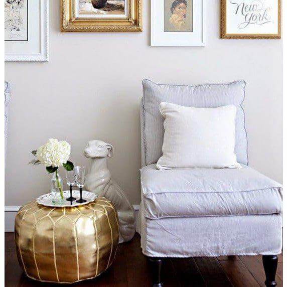 Stijlvolle woonkamer met Marokkaanse poef goud als decoratief voetenbankje naast een comfortabele witte stoel.