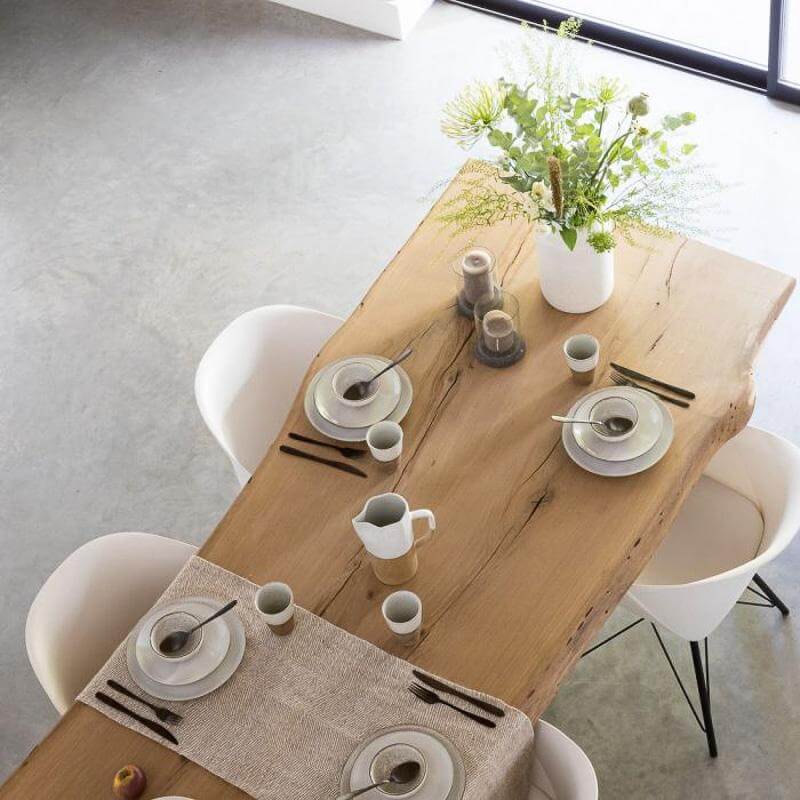 Moderne eetkamer met houten tafel, witte stoelen en elegant gedekte tafel met servies en bloemenvaas, ideaal voor ontbijt of diner.