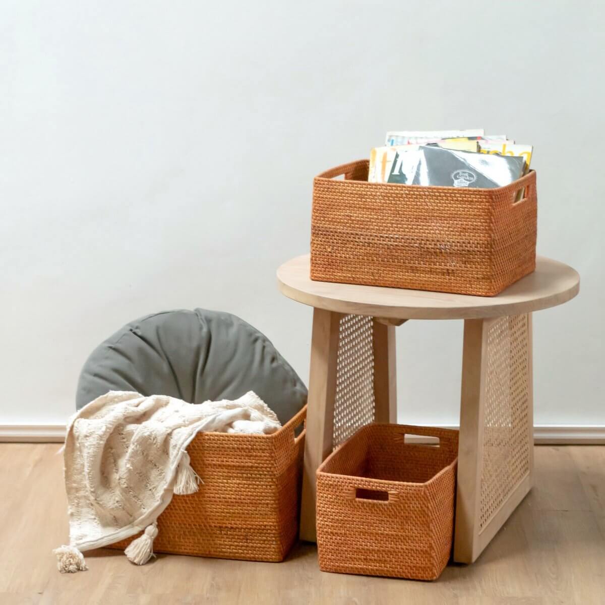 Drie roestkleurige rotan opbergmanden WARSA op tafel, perfect voor tijdschriften en speelgoed. Handgemaakt en milieuvriendelijk.
