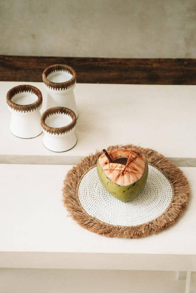 Tropische tafelschikking met raffia en zeegras placemat, kokosnoot in het midden, boho interieur accessoires, rustieke witte vazen.