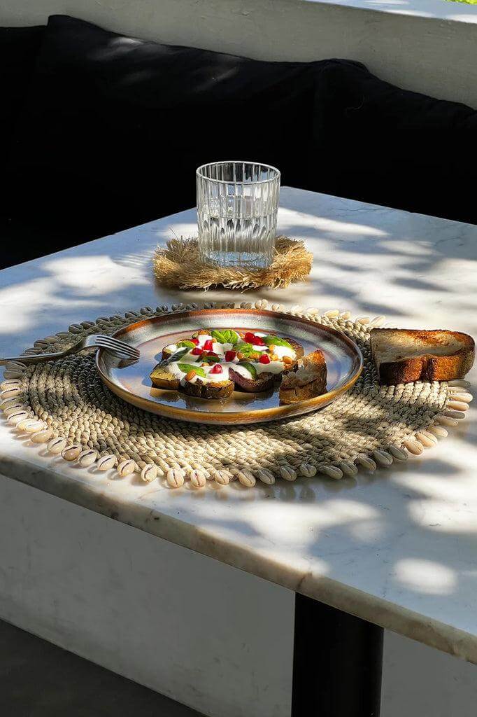 Tropische tafelsetting met zeegras placemat en kauri schelpen, stijlvolle toevoeging aan elke boho- of kustinterieur.