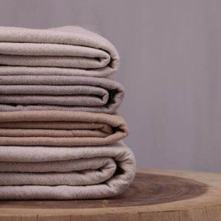 Gestapelde Pompom dekens in taupe op houten tafel, perfect voor boho en moderne interieurstijlen.