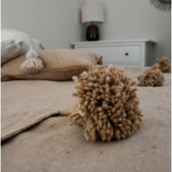 Marokkaanse beige pompomdeken op bed, interieurdecoratie met gezellige sfeer.