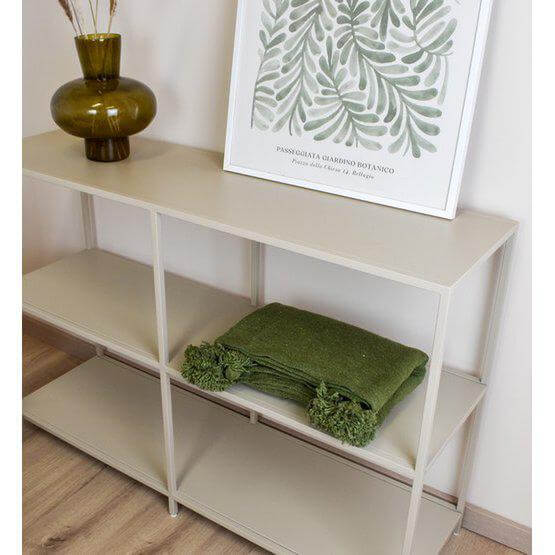 Groene Marokkaanse pompomdeken op een witte plank naast groene decoraties.