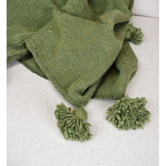 Groene Marokkaanse pompomdeken op een beige bank, perfect als stijlvol en gezellig interieur accent.
