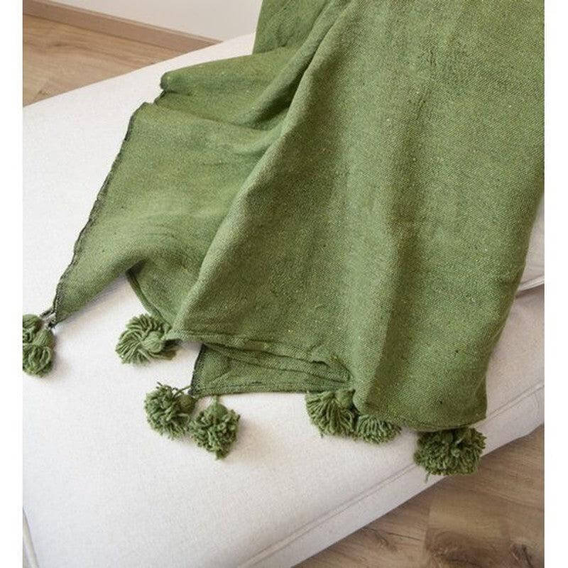 Groene Marokkaanse pom pom deken op witte bank, sfeervol en passend bij moderne en bohemien stijlen. Perfect voor slaapkamer of woonkamer.