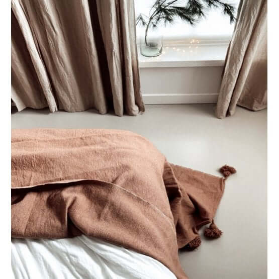 Marokkaanse Pompomdeken XL in beige camel op een bed, perfect voor een modern of bohemian interieur.