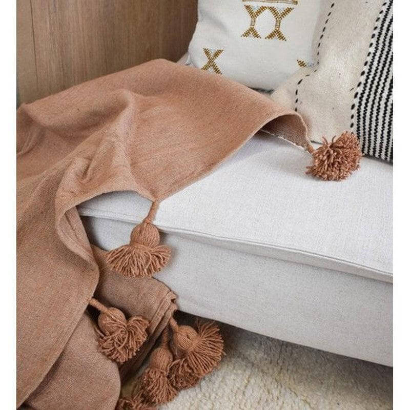 Marokkaanse pompomdeken in beige camel op een stijlvolle bank, perfect als statement piece voor elk interieur.