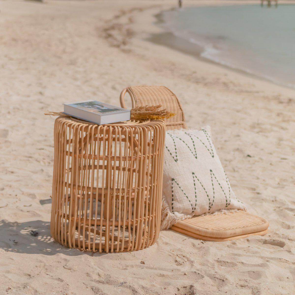 Handgemaakte rotan bijzettafel op het strand, ideaal als banktafel, met kussen en boek, 50 cm doorsnede en 55 cm hoog.