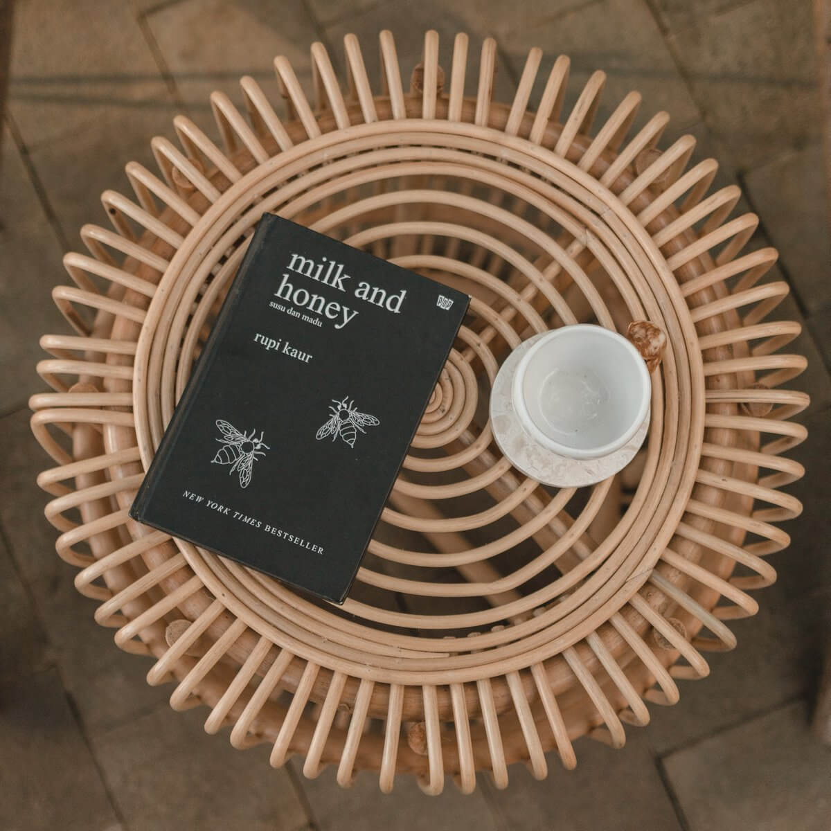 Rotan bijzettafel met 'Milk and Honey'-boek en koffie in keramische mok, perfect voor een gezellige hoek.