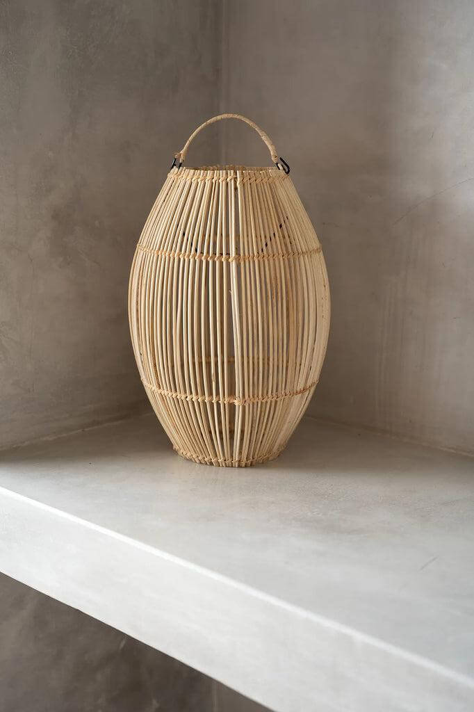 Rotan hanglamp The Zuri op een tafel, decoratieve klokvormige verlichting voor binnen of overdekte buitenruimtes.