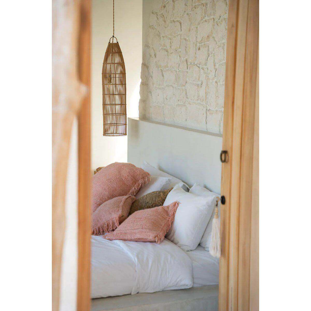 Sfeervolle slaapkamer met hangende rotan lamp 'The Fish Trap' in boho-stijl bij Bazar Bizar, warme uitstraling met kussens en oude muur.