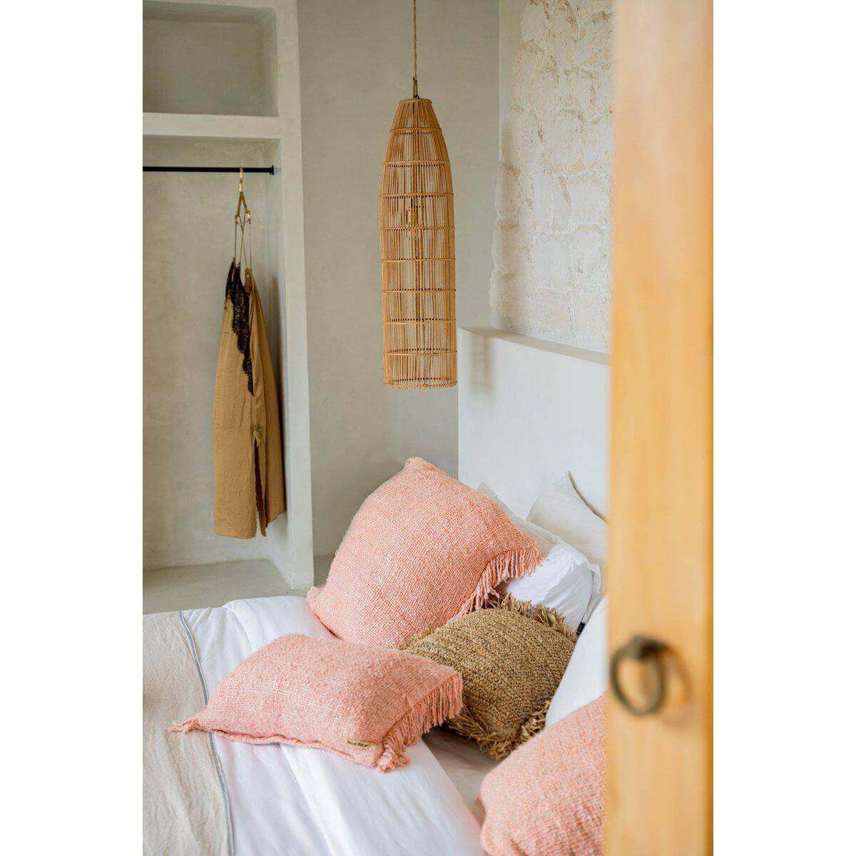 Rotan lamp The Fish Trap - L in een bohemian slaapkamer, stijlvol hangend boven roze kussens en een witte beddengoedset.