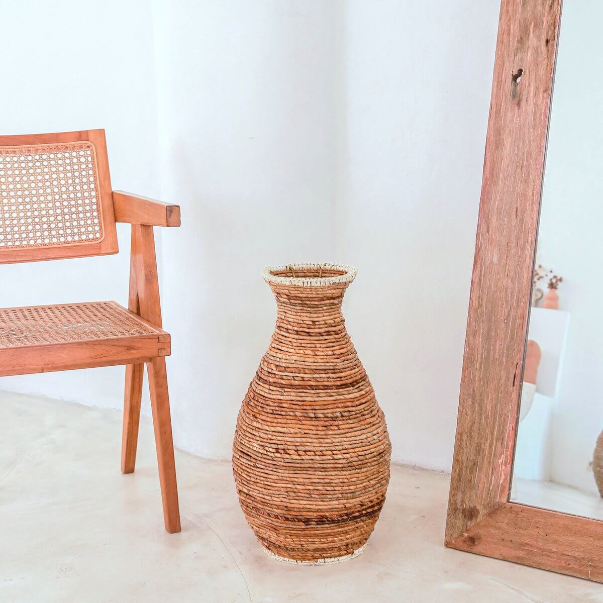 Grote natuurlijke vaas van robuust materiaal naast een houten stoel en spiegel.