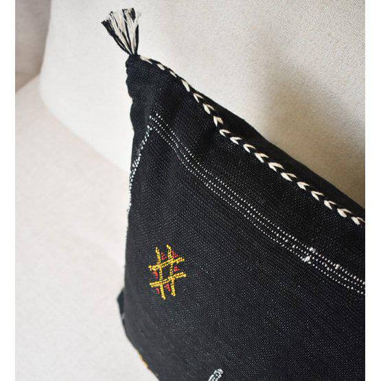 Zwart sabra kussen met bohemian patroon en natuurlijke kleurstoffen op een lichte bank voor een Ibiza sfeer.