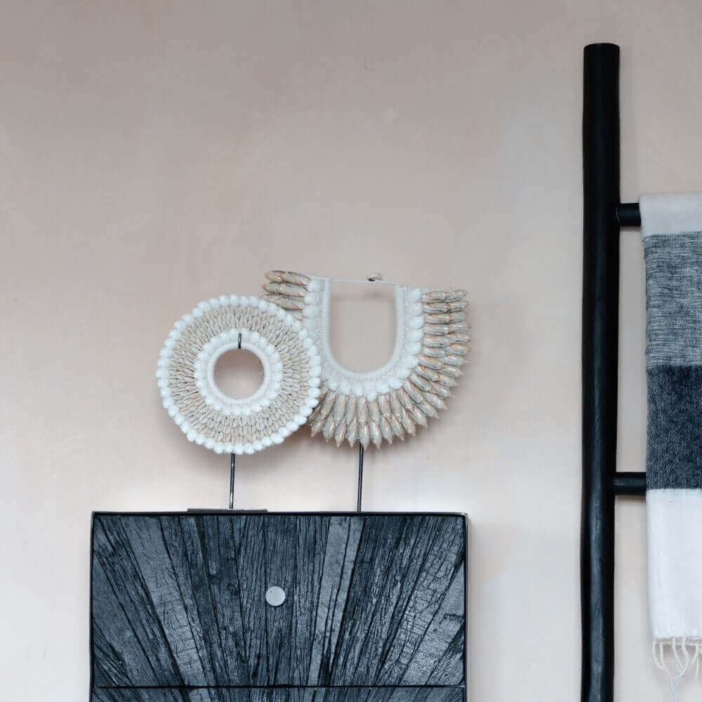 Handgemaakte schelpenketting op standaard, Melati collectie, tegen een neutrale muur voor een stijlvol interieurdisplay.