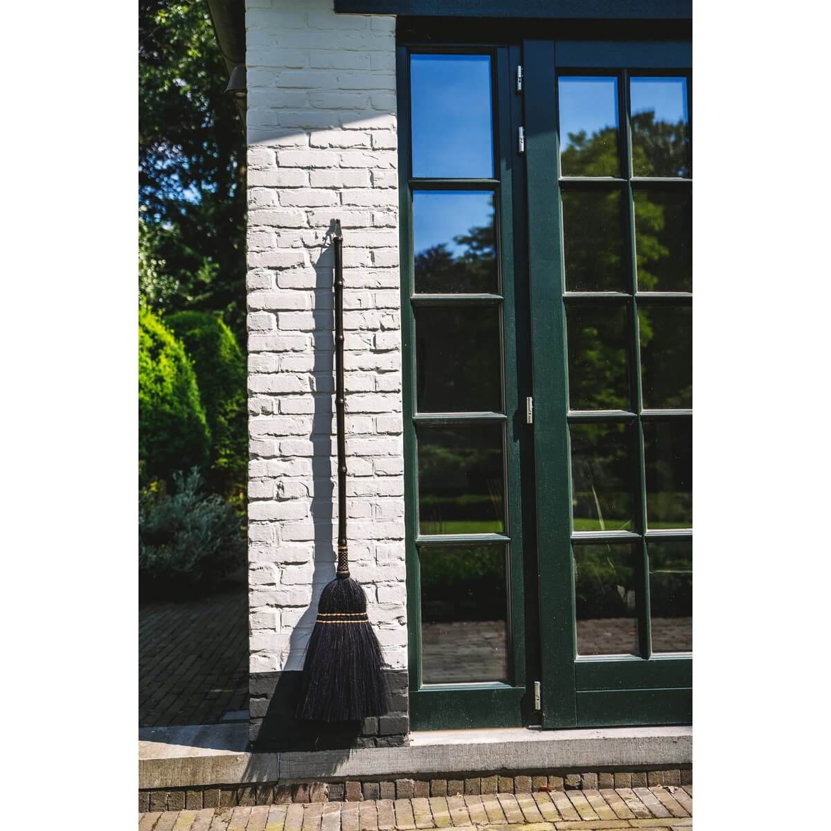 Bohemian black Indonesian grass broom leaning against a white brick wall in a garden setting.