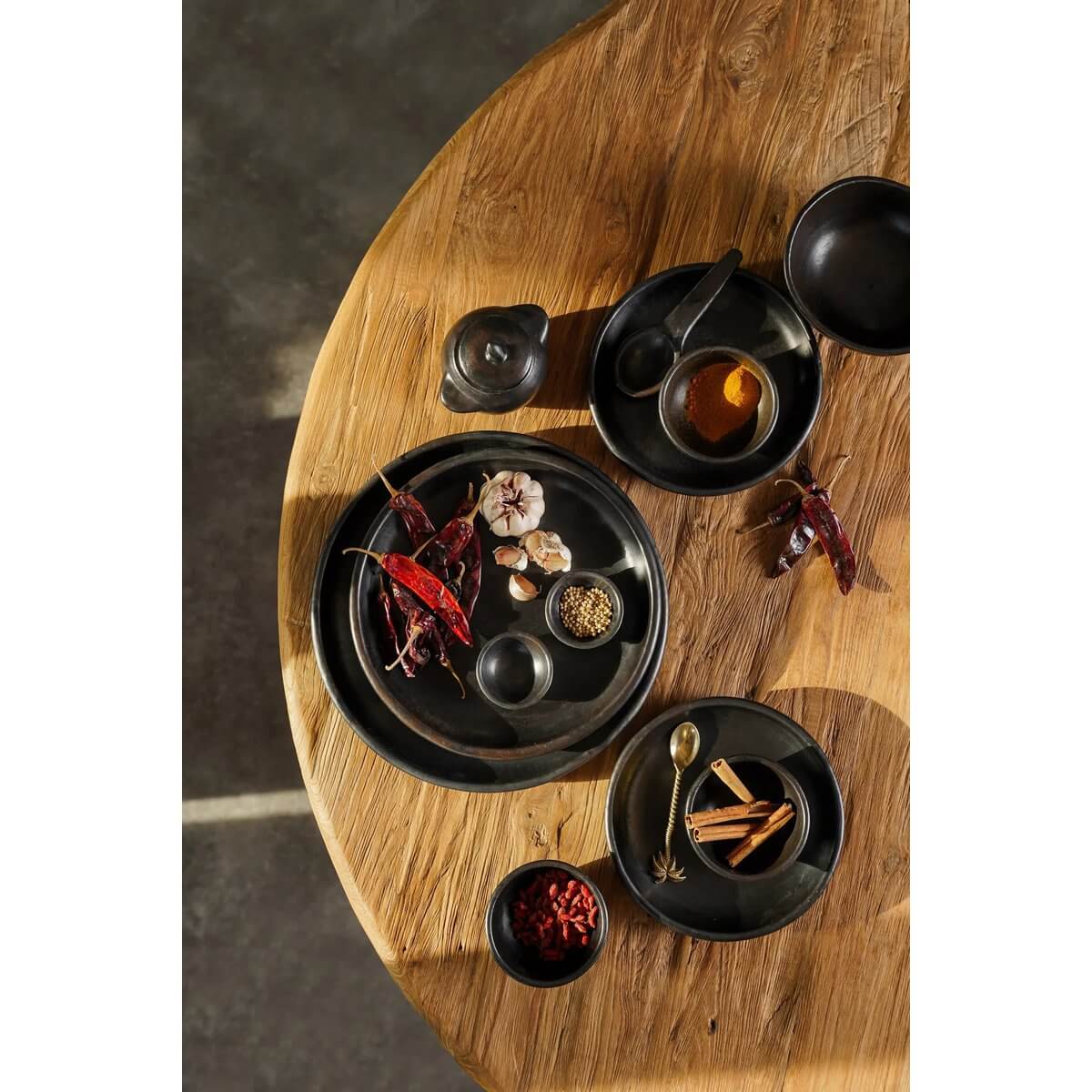 Bohemian-style black ceramic plates with spices on a wooden table, showcasing The Burned Classic Plate by Bazar Bizar Living.