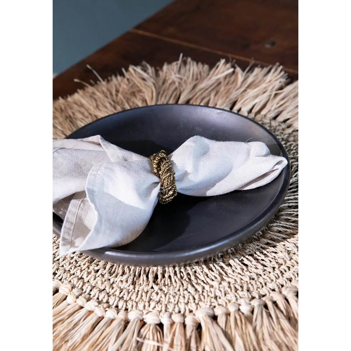 Bohemian black ceramic plate with napkin on straw placemat, perfect for stylish brunch or dinner setting.
