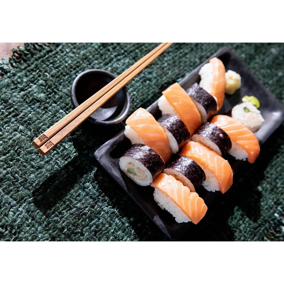 Delicious sushi rolls on a burnt black terracotta serving board, with chopsticks on the side, perfect for a Bohemian dining vibe.