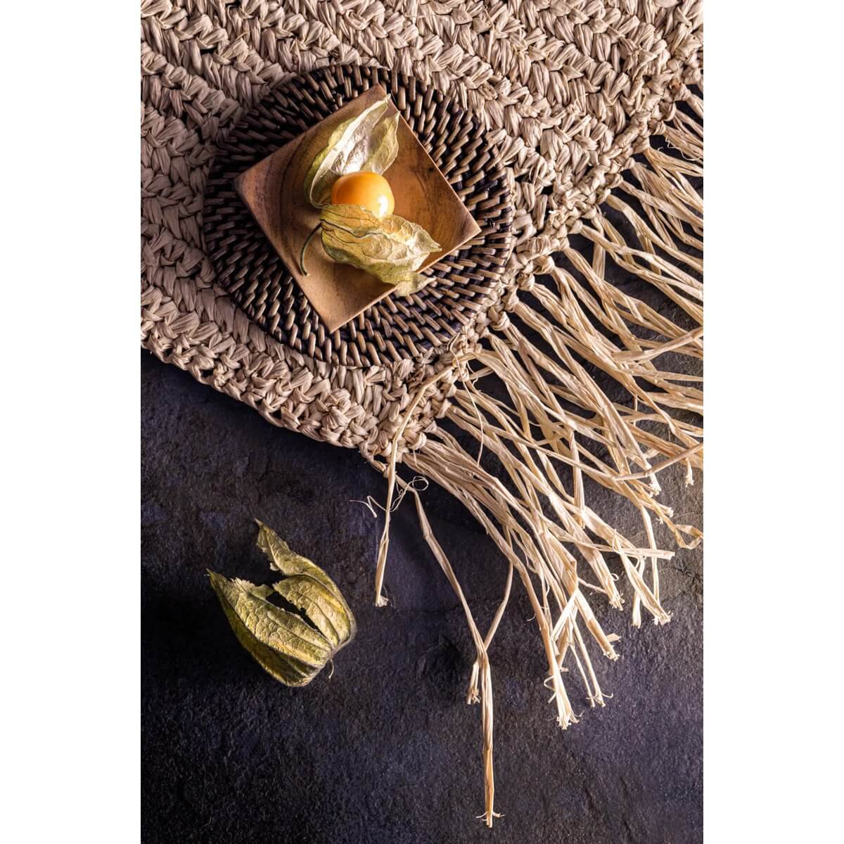 Bohemian handwoven rattan coaster on textured surface with decorative fruit, perfect for adding tropical flair to any table setting.