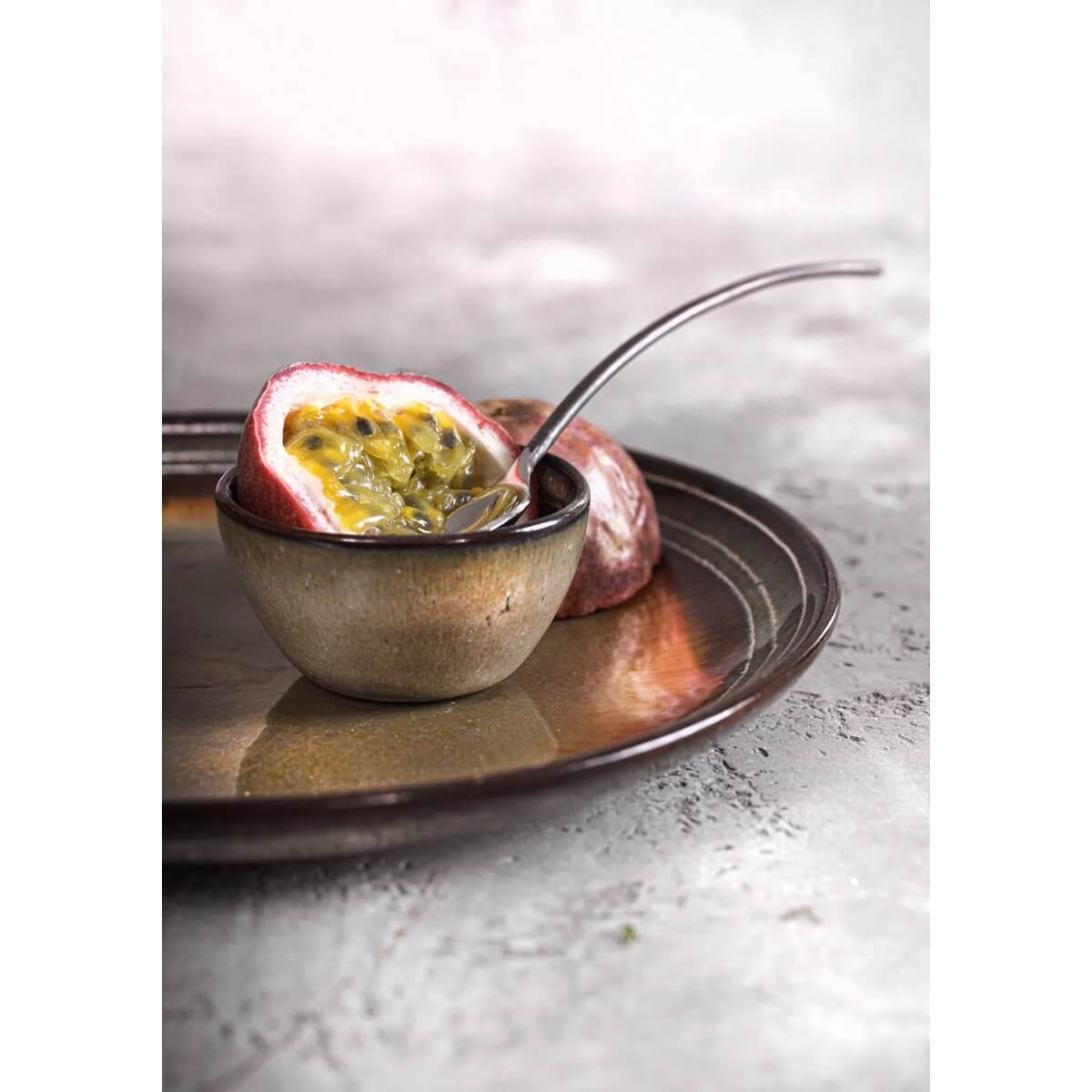 Passievrucht in keramisch schaaltje op rustieke schaal, sierlijk contrast tussen kleurrijk fruit en aardetinten servies.