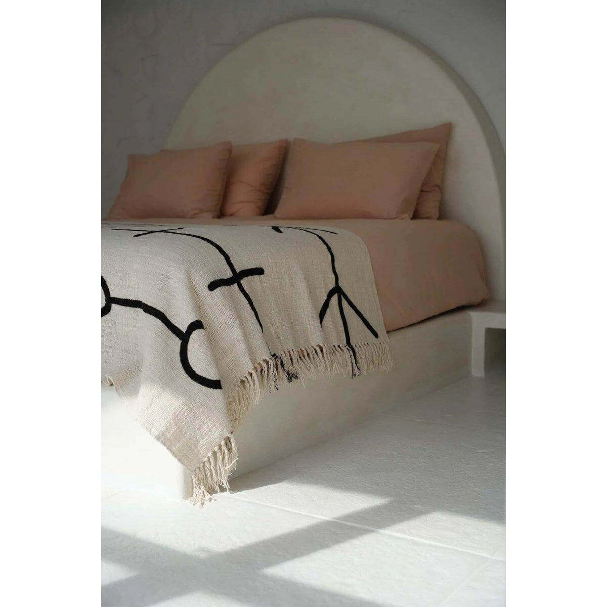 Natuurlijk zwarte Evil Eye bedsprei gedrapeerd over een bed, met mystieke symboliek en moderne elegantie in een verfijnd interieur.