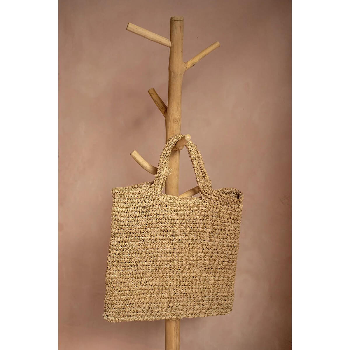 Natuurlijke Island Tote tas met geweven ontwerp, hangend aan houten rek. Perfect voor stranddagen en dagelijks gebruik. Stijlvol en duurzaam.
