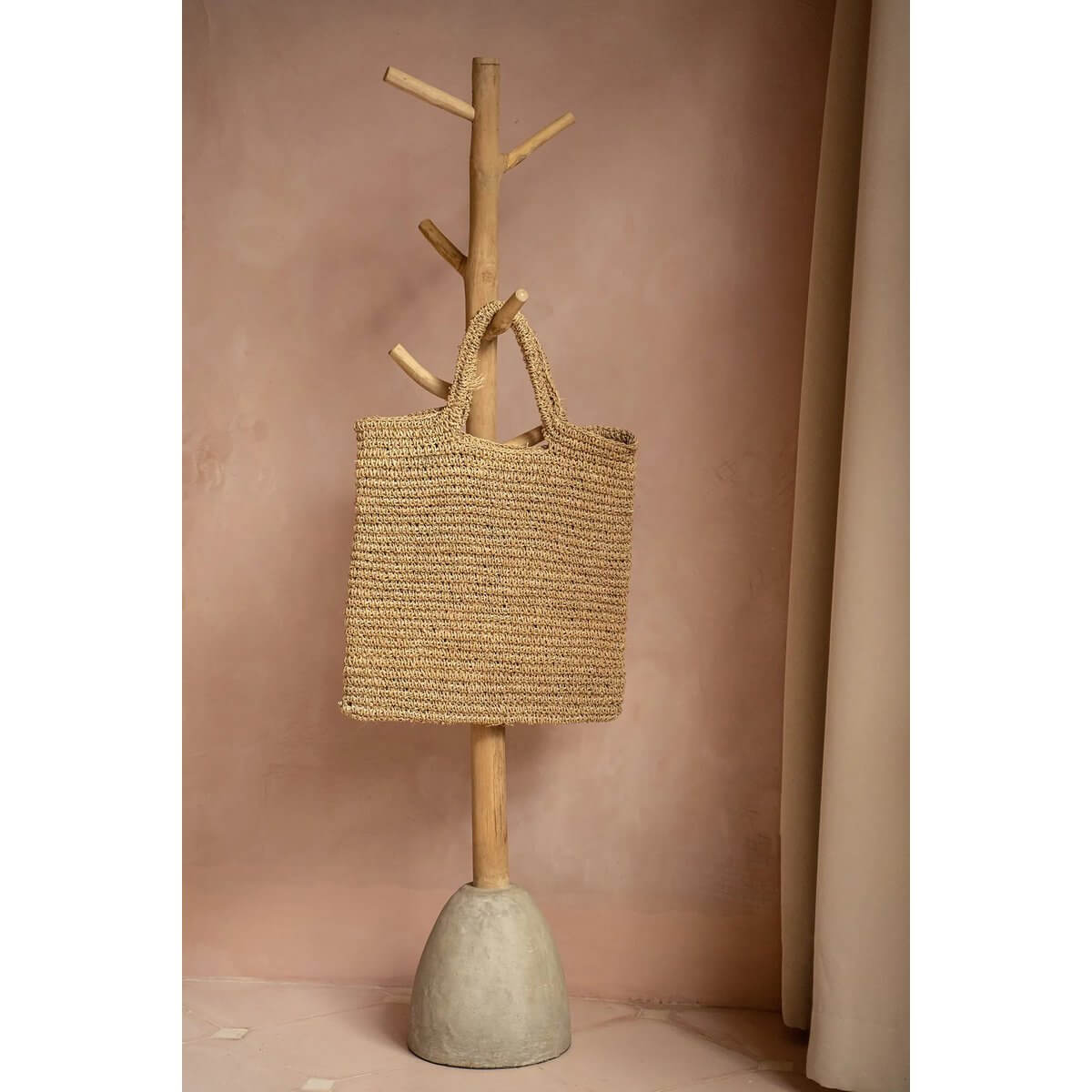 Alt Tag: The Island Tote - Natuurlijk, geweven strandtas hangend aan houten rek, perfect voor dagelijkse stijl en strandavonturen.