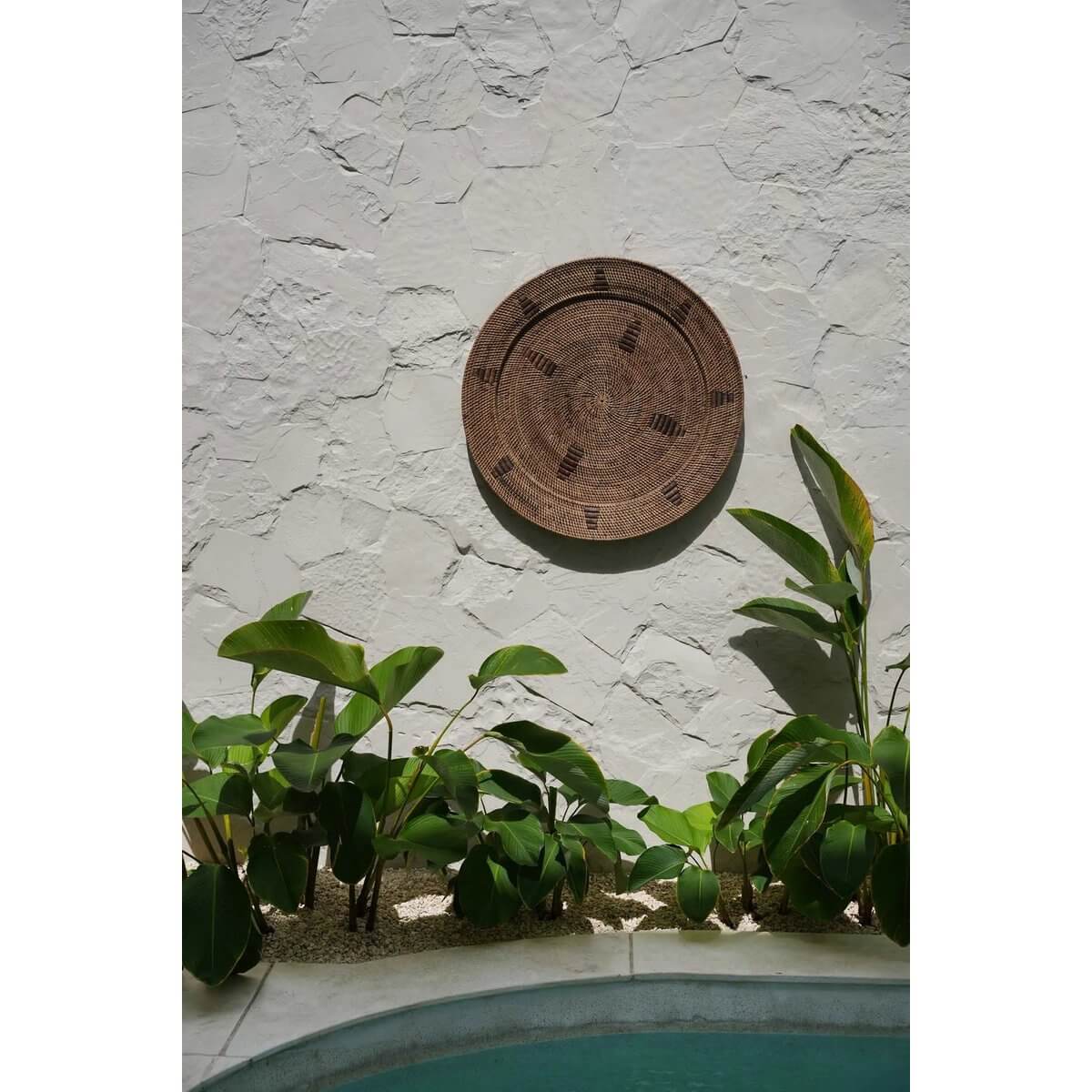 Alt Tag: Handgeweven bruin en zwart rotan bord, 60cm breed, met etnische patronen, aan muur op tuin, merk Bazar Bizar Living.