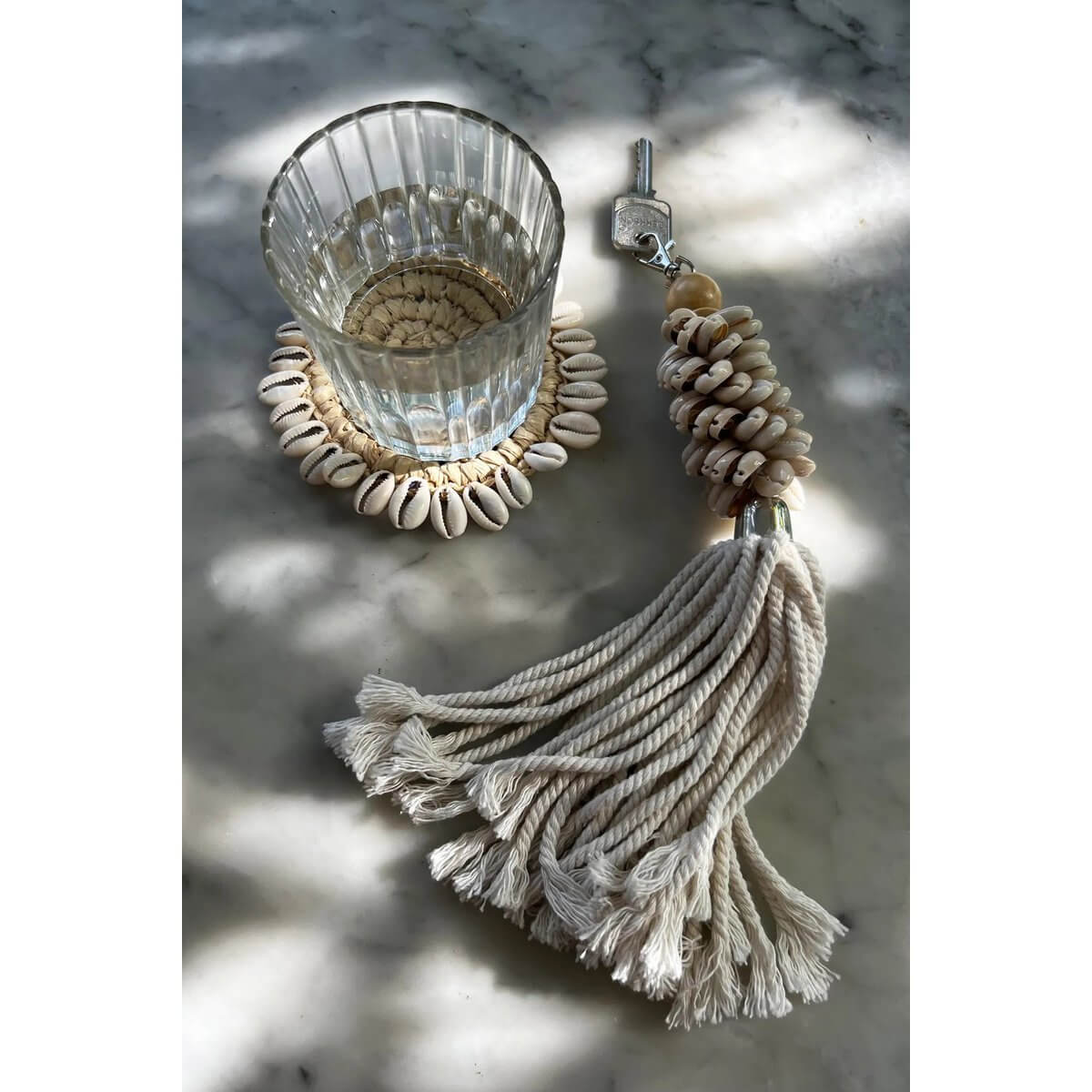 Glass on Bohemian Raffia Shell Coaster with Key Tassel Decor, enhancing table décor with Balinese shell design flair.