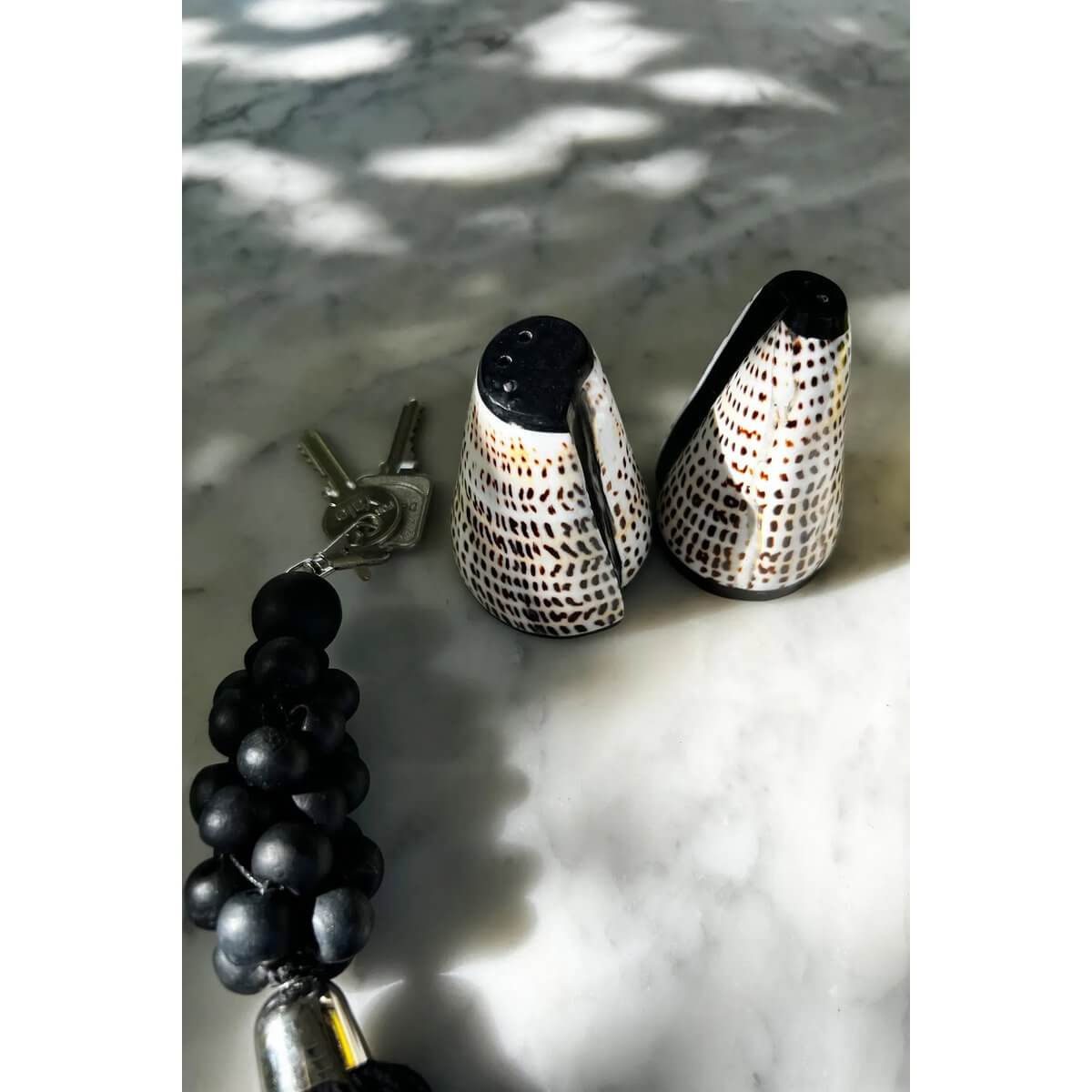 Bohemian Salt and Peppa Shell Set on marble, handmade from shells with black details, perfect for elegant dining by Bazar Bizar Living.