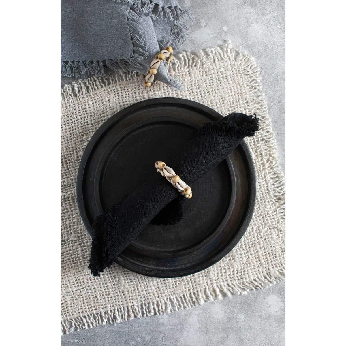 Bohemian black napkin with shell napkin ring on rustic plate, part of The Shell Servetring Set of 4, by Bazar Bizar Living.