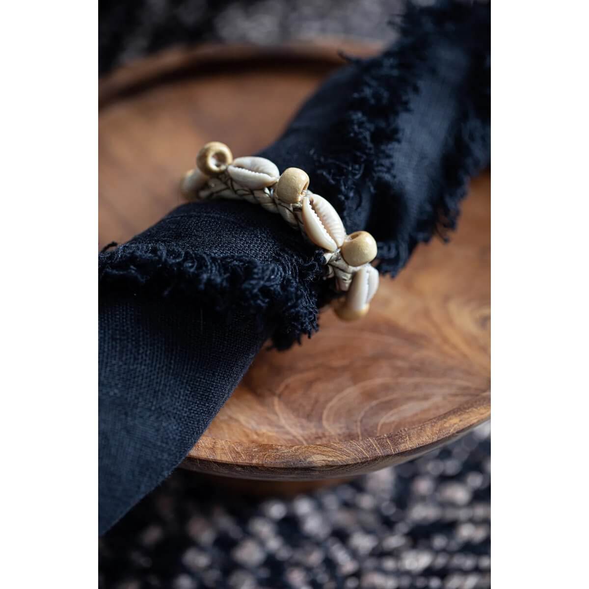 Bohemian-style napkin ring adorned with shells from Bazar Bizar Living, displayed on a wooden plate for elegant table decor.