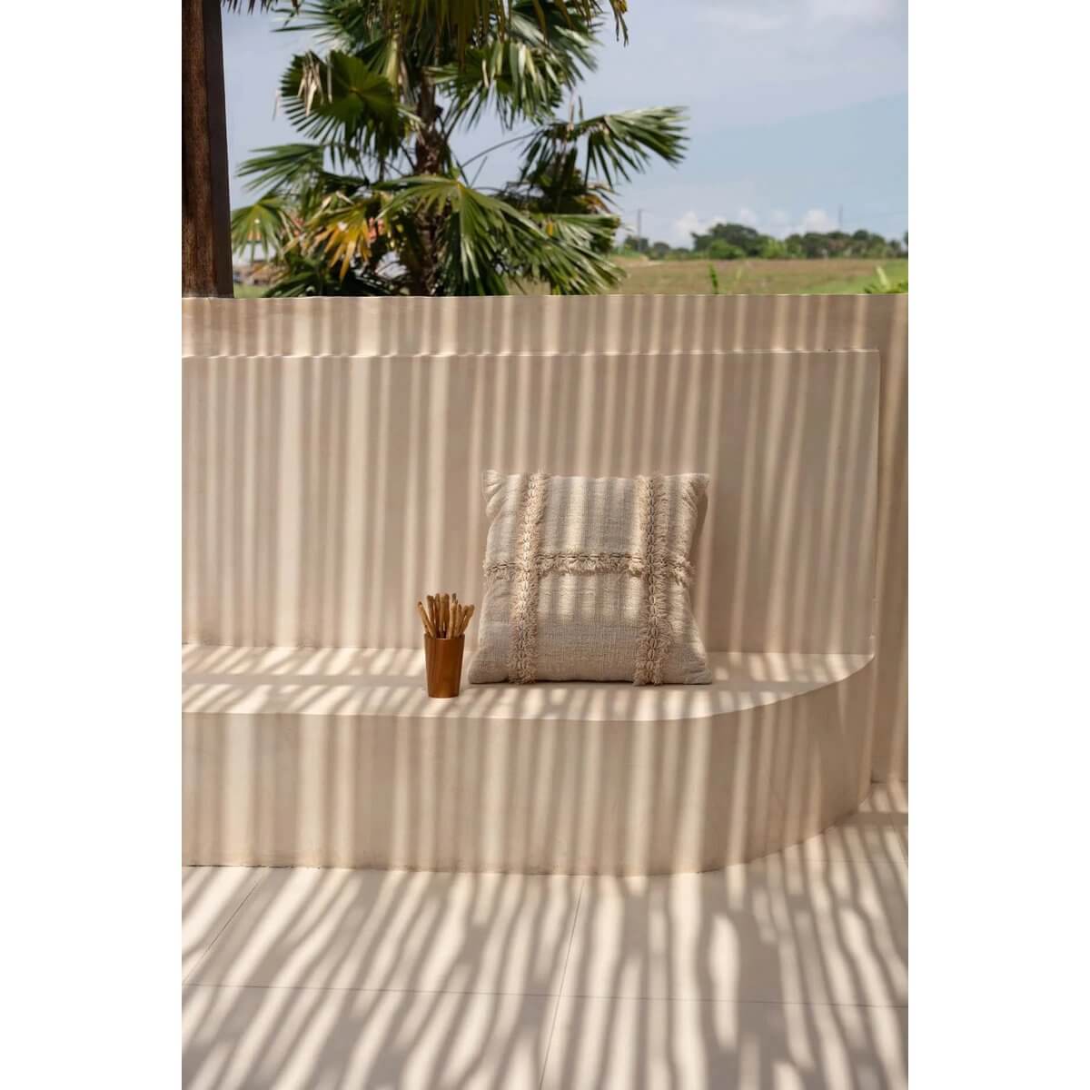 Bohemian outdoor setting with a Teak Root Cup and decorative pillow on a sunlit patio bench with palm trees in the background.