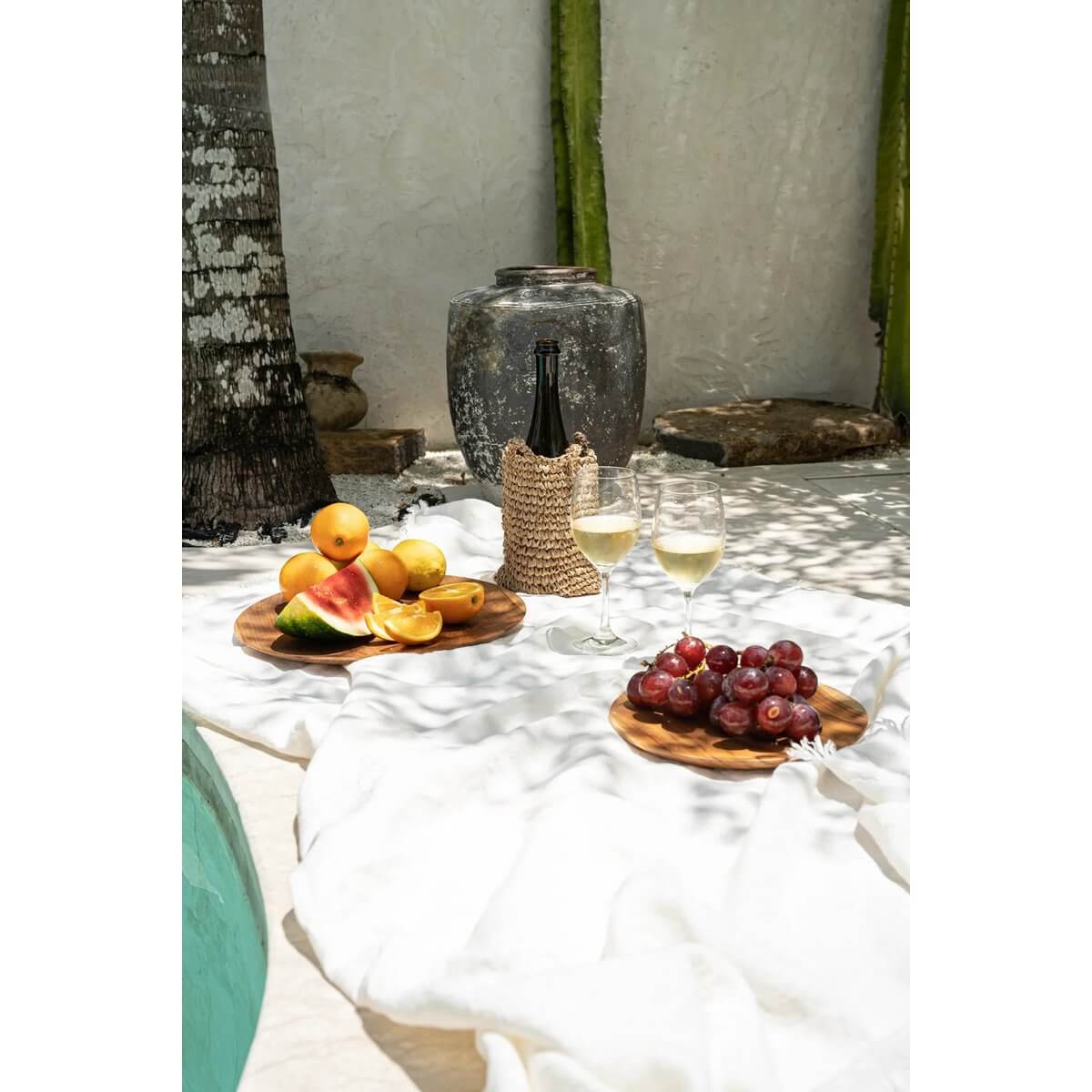 Bohemian picnic with Teak Root Round Plate serving fruit, wine, and grapes under a cozy outdoor setting.